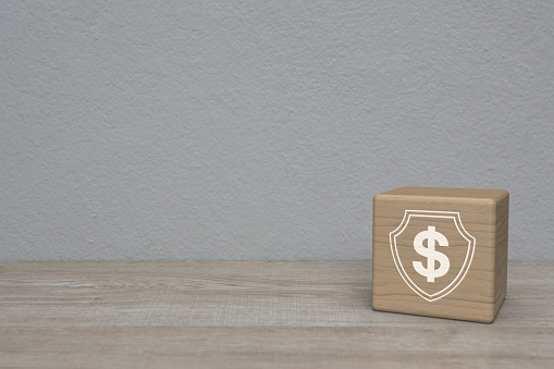 Dollar with shield flat icon on block cube on wooden table over white wall background, Business money insurance and protection concept