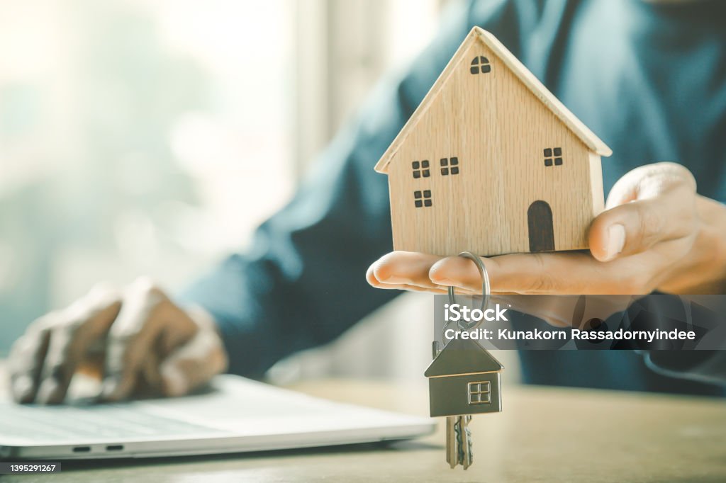 Businessman choosing mini wood house model from model and row of coin money on wood table, selective focus, Planning to buy property. Choose what's the best. A symbol for construction ,ecology, loan concepts. Home Ownership Stock Photo