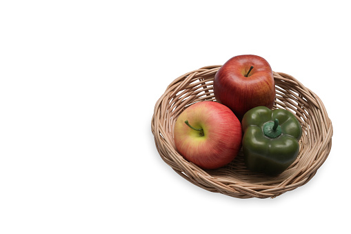 Red apples and sweet pepper in wicker basket isolated on white background.