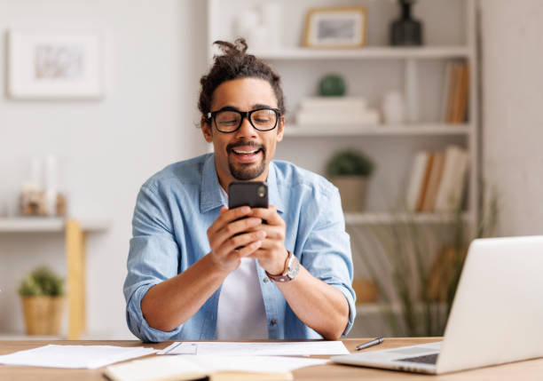 istock Young african american man freelancer working remotely on laptop and browsing smartphone or studying online at home 1395293191