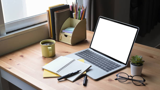 istock Computer laptop with white screen, coffee cup and supplies on wooden table. 1395293365