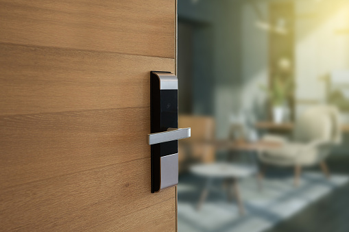 Digital door lock installed on wood door for security and access the room. Door wood texture with electronic door lock opened in front of blur living room.