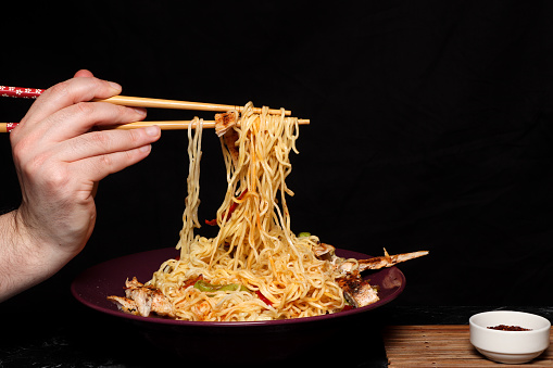 Vegetable noodles served with chunks of grilled chicken meat.Black background.