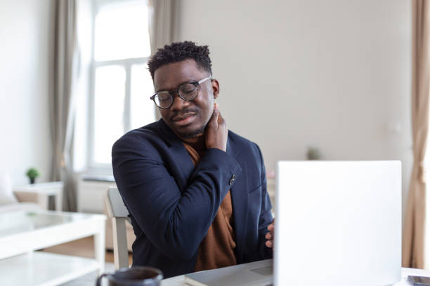 istock Feeling exhausted. Frustrated young handsome man looking exhausted while sitting at his home and working on his laptop while massaging his neck, Neck pain 1395296302