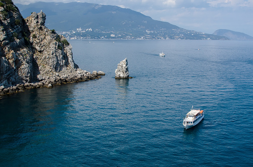 Landscape in Yalta in summer. A white boat is sailing on the black sea, gray rocks and mountains. Backgrounds