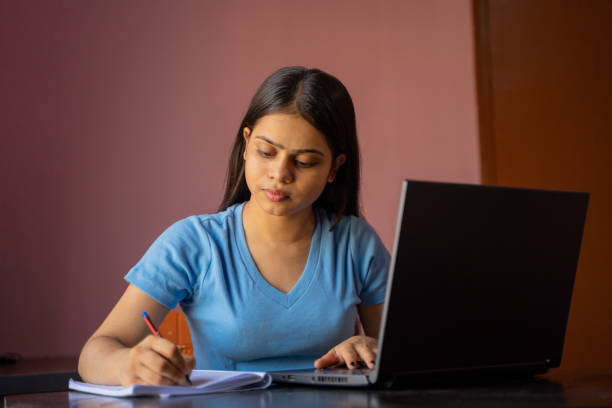 istock Indian girl sitting at the desk studying or working on laptop making notes 1395297061