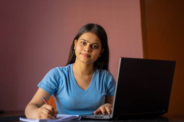 istock Indian girl sitting at the desk studying or working on laptop making notes 1395297064