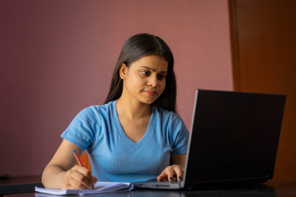 istock Indian girl sitting at the desk studying or working on laptop making notes 1395297105