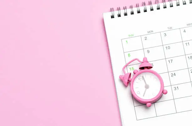 Pink alarm clock and calendar on a pink background. Concept days of menstruation or menopause. Template Copy space for text. mock-up.
