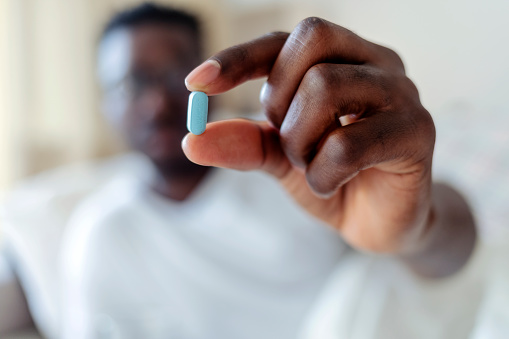 Photo of Sick young African man holding pill and glass of water at home. Cropped shot of a young man taking medication at home.