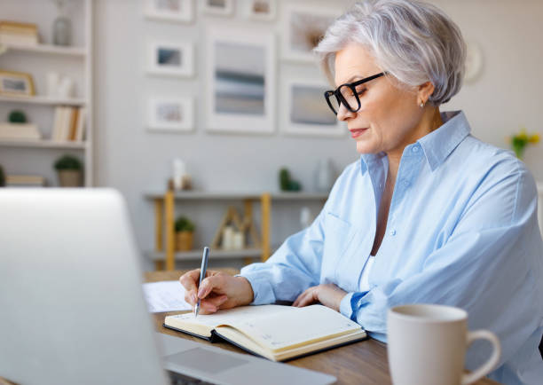 istock Mature businesswoman working at laptop, reading documents and take notes in home office 1395298516