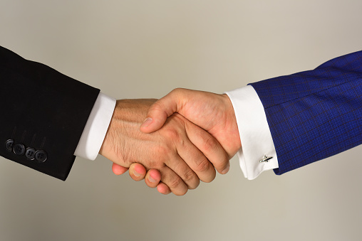 Close-up Of Doctor And Businessman Shaking Hands On Grey Background