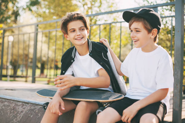 due simpatici adolescenti si siedono in uno skatepark, si rilassano dopo lo skateboard e chiacchierano. i ragazzi si godono il loro tempo libero nello skate park, seduti sulla rampa. il concetto di gioventù, unità e amicizia - skateboard park extreme sports recreational pursuit skateboarding foto e immagini stock