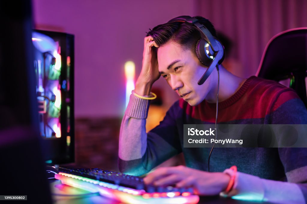 asian gamer is upset Professional young asian male gamer playing online on his PC in the living room at night - He upset because of losing the game Gamer Stock Photo