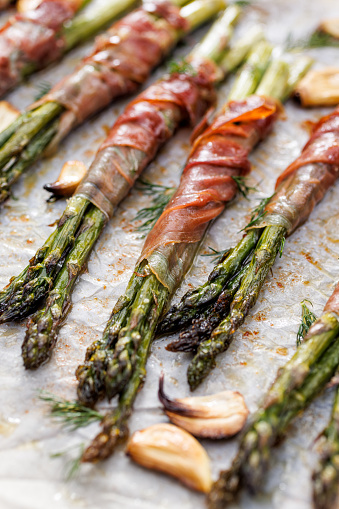 Roasted green asparagus wrapped with ham sprinkled with herbs, top view