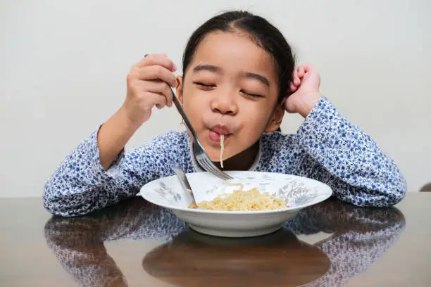 Asian kid showing happy expression when eating noodle