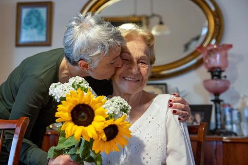 White-haired woman giving flowers and kissing her mother on mother's day at home