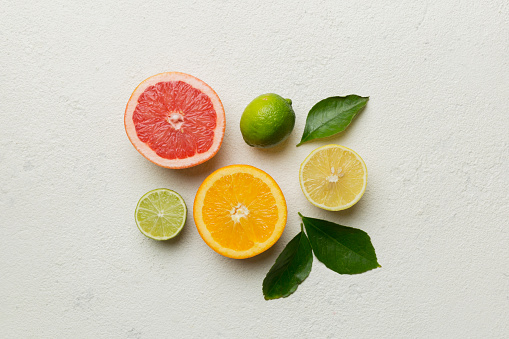 Stock photo showing citrus fruit slices on white background, modern minimalist photo of circular sliced pink grapefruit, oranges, lemon and lime citrus fruits showing segments, seeds / pips and rind around edge with leaves, healthy eating poster wallpaper background design.