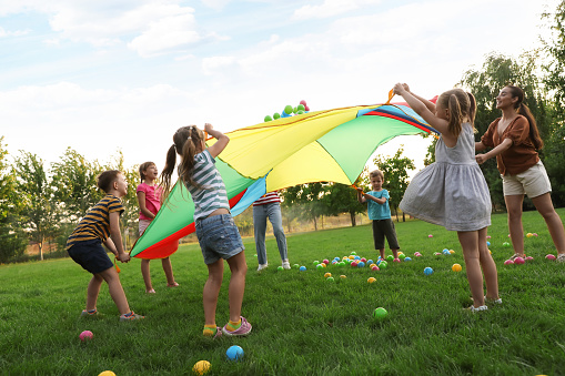 Grupo de niños y profesor jugando con el paracaídas arco iris del parque infantil sobre hierba verde. Actividad de campamento de verano photo