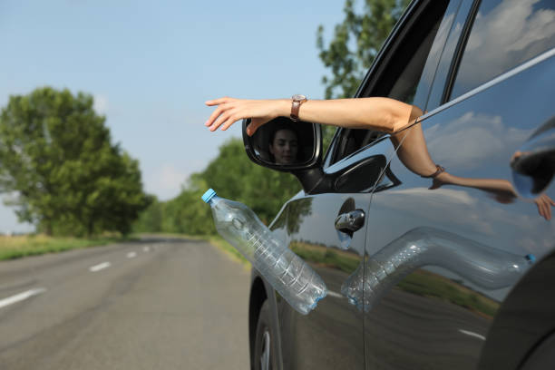 istock Driver throwing away plastic bottle from car window. Garbage on road 1395306022