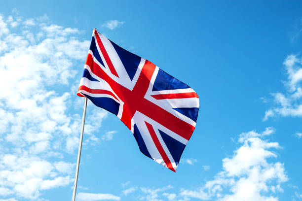 istock Great Britain England  flag waving in the wind over blue sky 1395310233