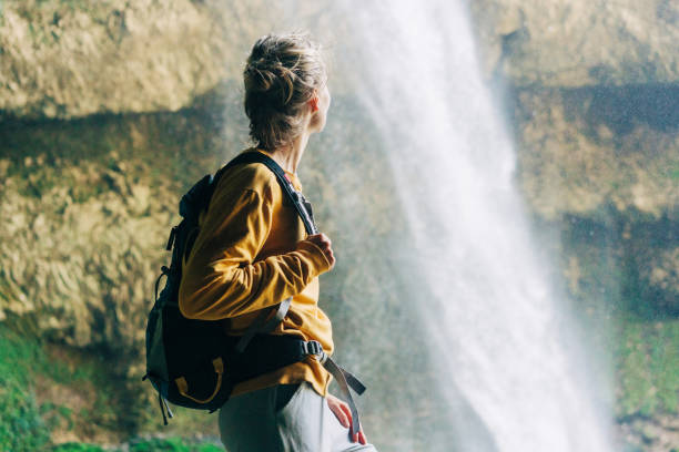 istock Woman hiker with a backpack in a mountain canyon near a large waterfall. 1395312072