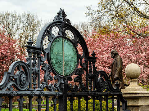 Boston, Massachusetts, USA - April 27, 2022: Close-up of Boston Public Garden's East Gate, Charles Street entrance. Early Spring view of Garden with the bronze statue of Edward Everett Hale in the background.