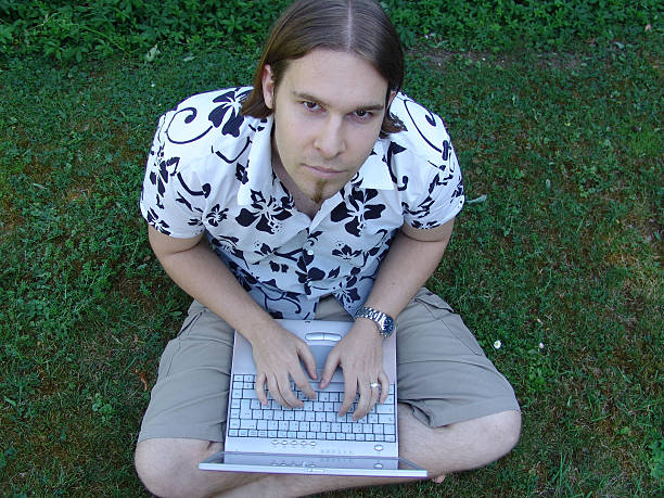 Young man sitting on grass with laptop stock photo