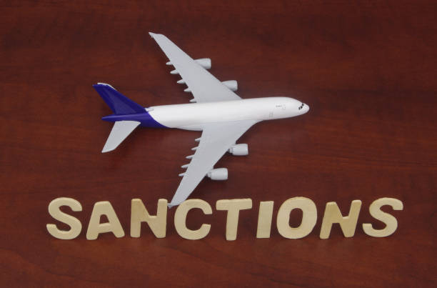 istock Airplane model with word sanctions on wooden background. 1395317319