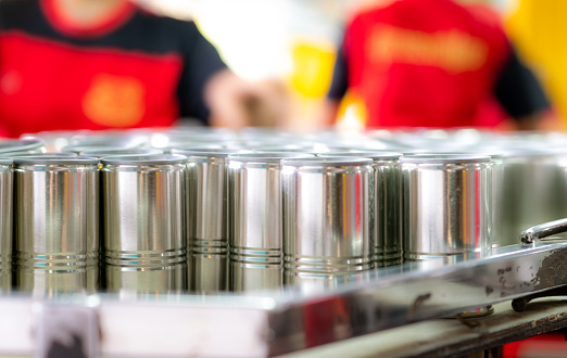 Many cans on blur workers. Canned fish factory. Food industry. Workers working in canned food factories to fill sardines in tinned cans. Food processing production line. Food manufacturing industry.