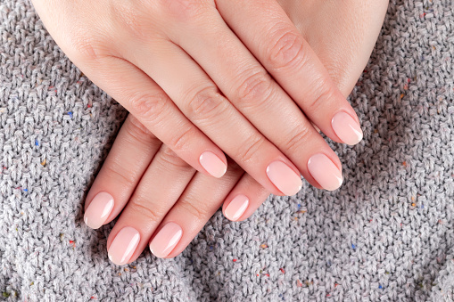 Female hands with beautiful natural manicure - pink nude nails on gray knitted fabric background. Nail care concept