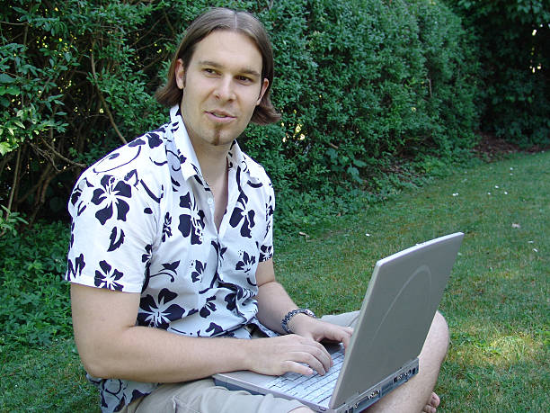 Young man sitting on grass with laptop stock photo