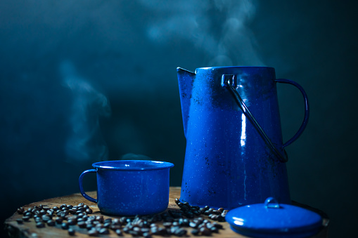 Enameled mug of coffee with smoke. set of coffee with pot and coffee bean on the old wooden floor. soft focus.