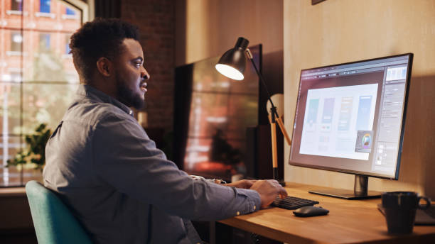 istock Young Handsome African American Man Working from Home on Desktop Computer in Sunny Stylish Loft Apartment. Creative Male Checking Social Media, Browsing Internet. Urban City View from Big Window. 1395320922