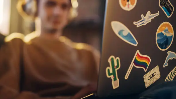 Photo of Close Up Footage of Person Using Laptop Computer with Diverse LGBT and Lifestyle Stickers on the Back. Creative Designer Typing on Keyboard, Browsing Internet and Checking Social Media.