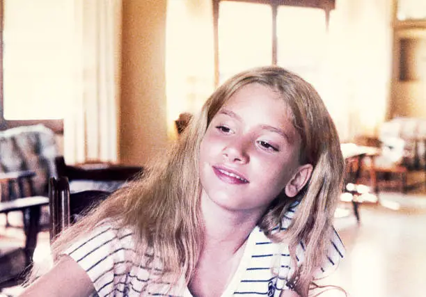 Analog photo of a blonde young girl smiling and looking away from the camera. Grainy image from the eighties.