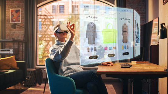 Young Beatiful Women está utilizando auriculares de realidad virtual para hacer compras en línea en un elegante apartamento tipo loft. La mujer vestida casualmente está usando ropa blanda innovadora para comprar tela. Concepto de sitio web 3D. photo