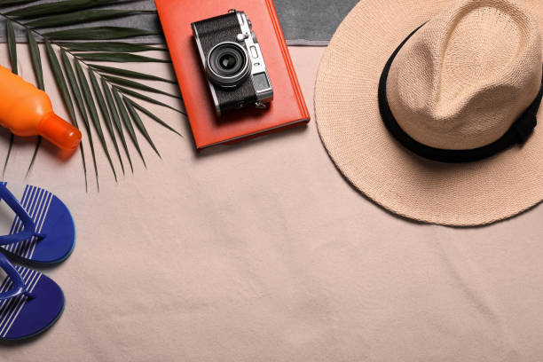 istock Beach towel, hat, book, camera, sunscreen, flip flops and tropical leaf on sand, flat lay. Space for text 1395322440