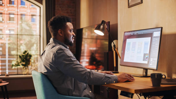 istock Young Handsome African American Man Working from Home on Desktop Computer in Sunny Stylish Loft Apartment. Creative Male Checking Social Media, Browsing Internet. Urban City View from Big Window. 1395322468