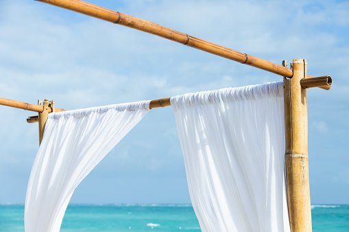 An empty gazebo fragment with white curtains on a bamboo frame is on a sandy beach, Dominican Republic, Bavaro beach