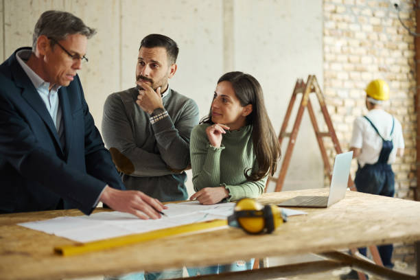istock Young couple and their agent examining blueprints at construction site. 1395324914