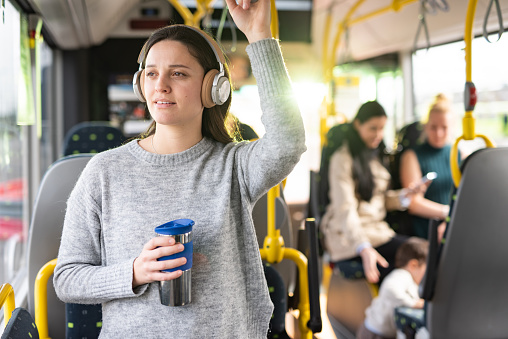 Young woman whit headphones standing in a bus and holding coffee