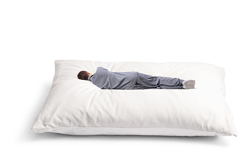 Rear view shot of a man in pajamas sleeping on a big pillow isolated on white background