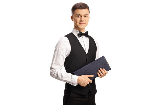 Young waiter with a bow tie looking at camera and holding a menu isolated on white background