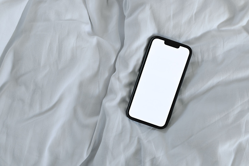 Smartphone mockup screen on white bed sheet, top view flat lay
