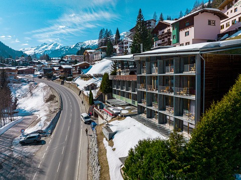 St. Anton am Arlberg. March 10, 2022. Hotel lux alpinae on sunny day in town. High angle view of luxurious ski resort against snowcapped mountains. Empty road leading towards village during winter.
