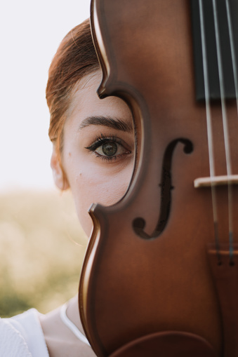 Ginger hair beautiful young woman with violin on half of her face. Looking at camera.