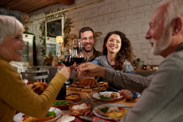 Celebratory toast during dinner time! Young happy couple toasting with senior couple while enjoying in lunch at dining room. father in law stock pictures, royalty-free photos & images