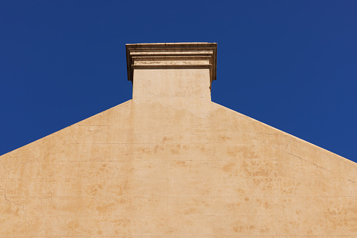 Close-up on a side wall of a building with chimney and deep blue sky beyond.