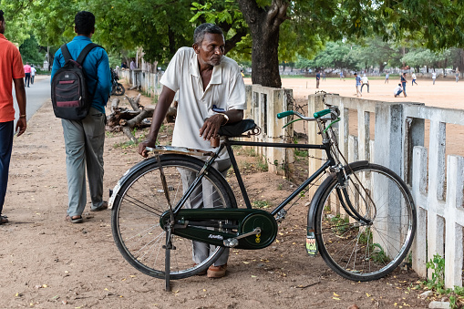 Vellore, Tamil Nadu, India - September 2018: An Indian man standing beside his bicycle and staring thoughtfully.